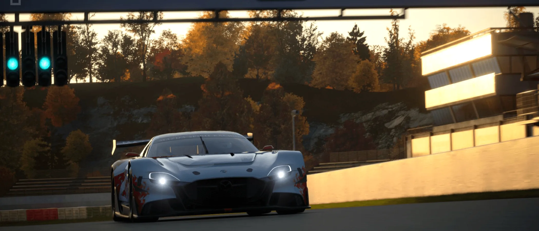 A racing car approaches a corner on an autumnal Gran Turismo 7 circuit at sunset.